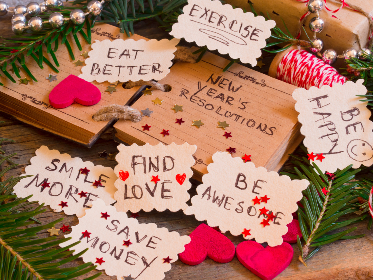 'New Year's Resolutions' on Calendar Book Surrounded by Written Goals and Confetti